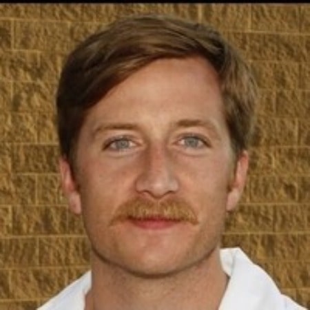 kyle-Baugher was wearing white cloths. He has brown mustache.